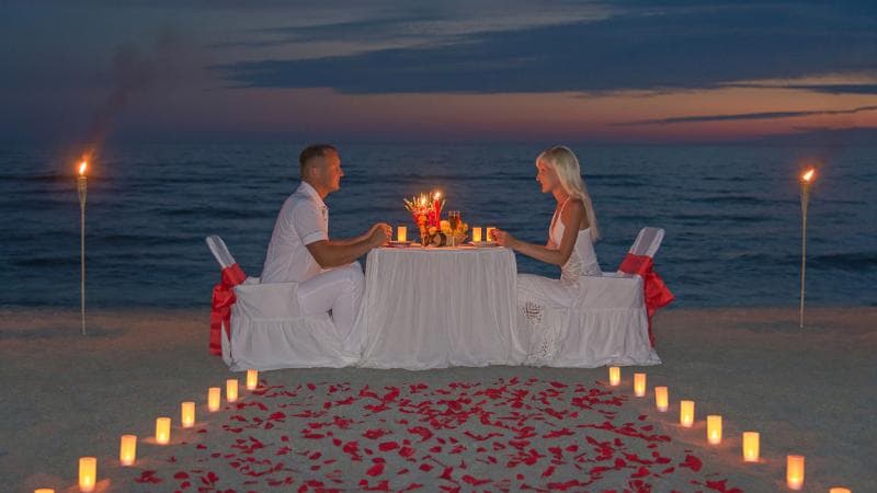 A couple sharing a candlelit dinner on the beach